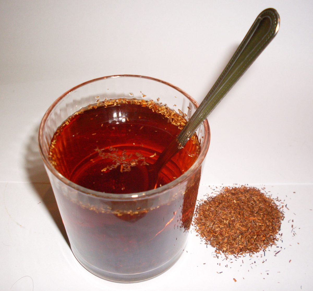 A glass of brewed red rooibos beside a small heap of dry rooibos leaf