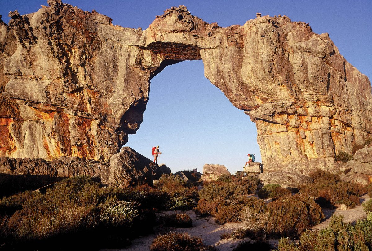 Two hikers standing beneath the Wolfberg Arch, a natural sandstone arch in the Cederberg